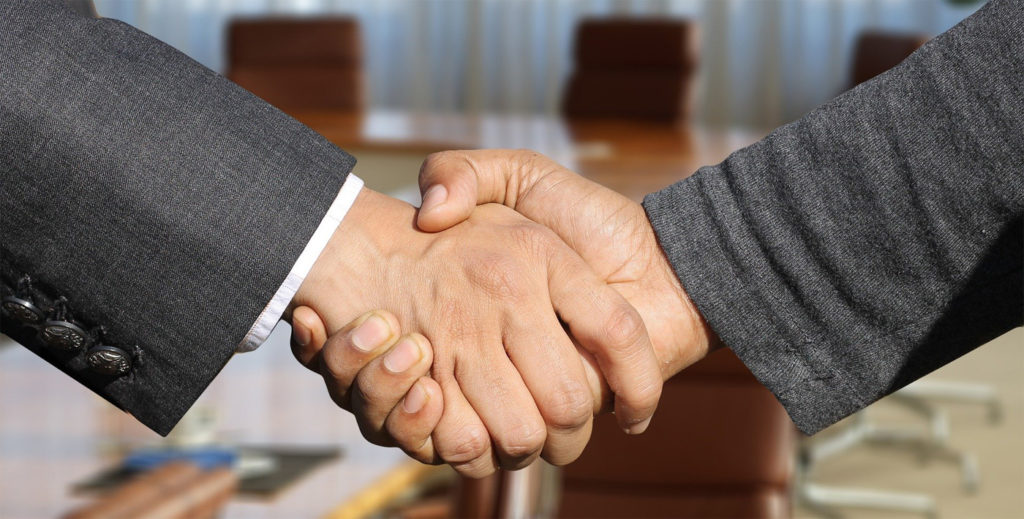 Two person are handshaking inside a meeting room